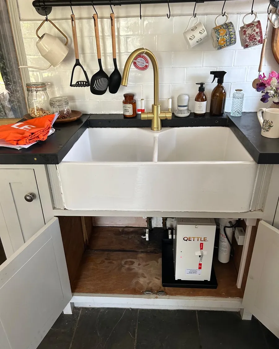 Brass tap over a double Belfast sink with the cupboard open, showing the boiler tank fitted underneath