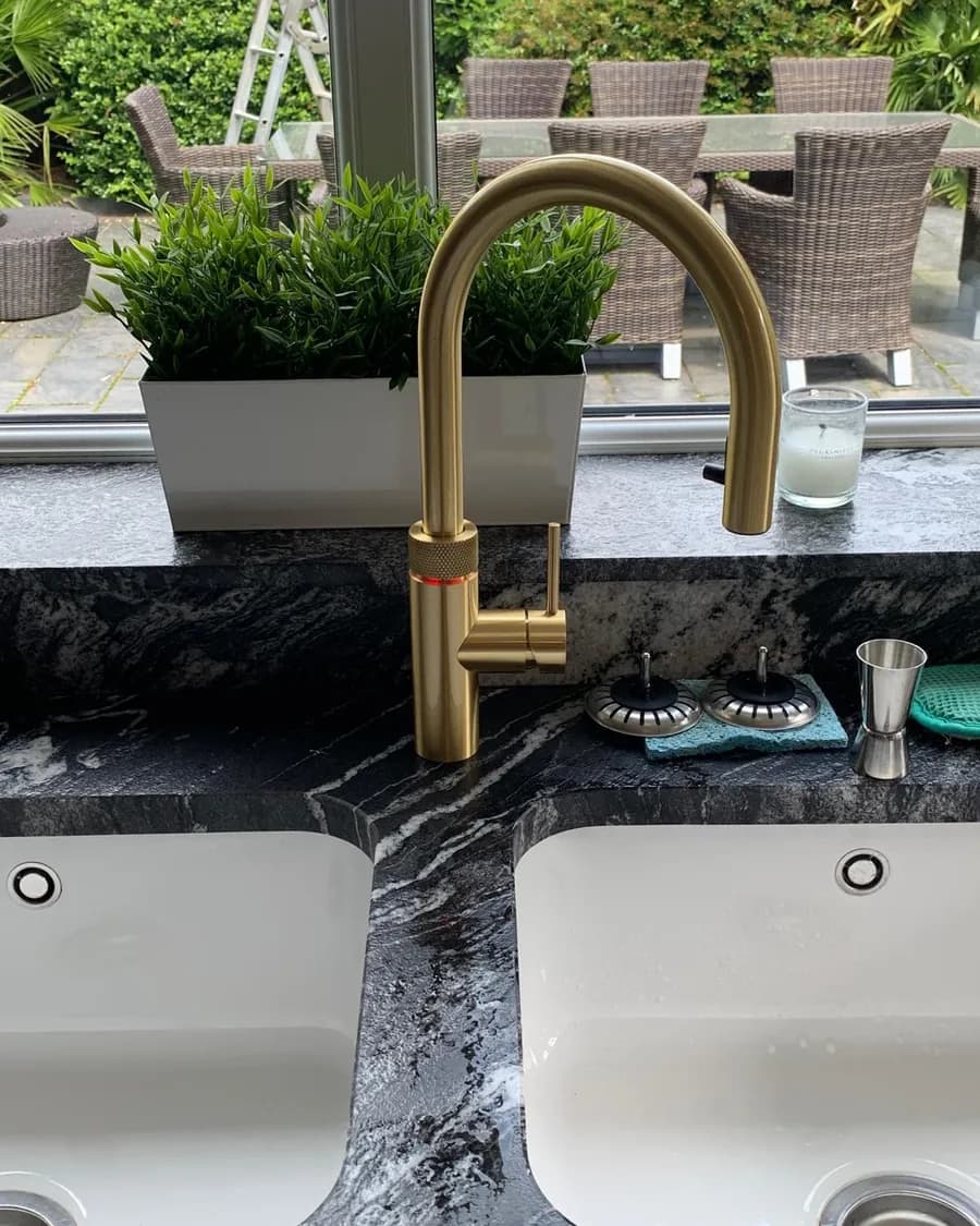 Brushed gold boiling water tap on a dark granite worktop by a garden window